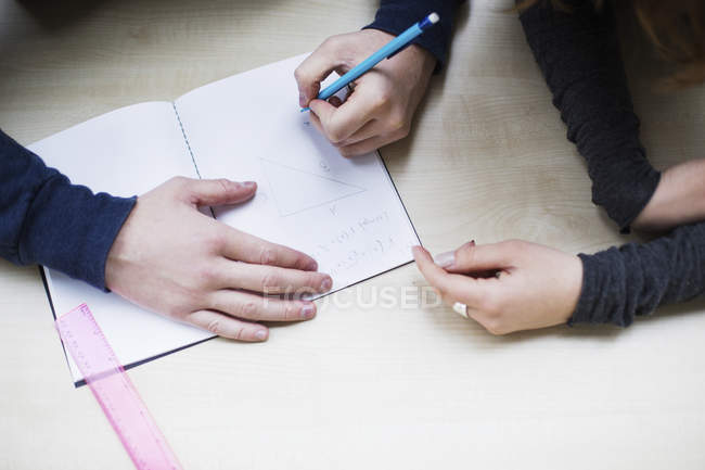 Close-up view of students writing in notebook at desk in classroom — Stock Photo