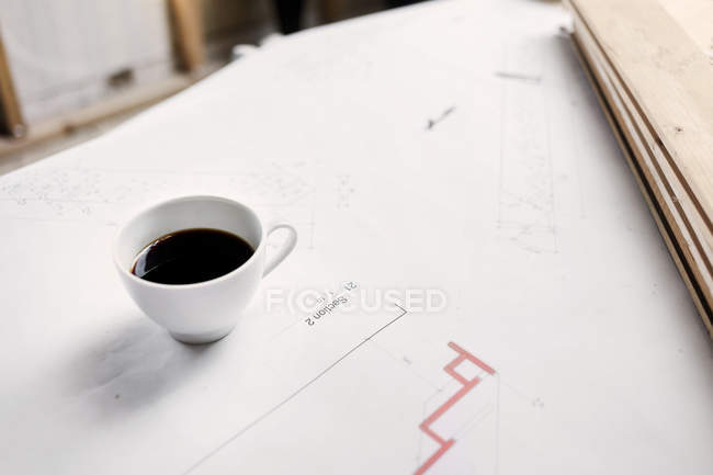 Coffee cup standing on blueprints — Stock Photo