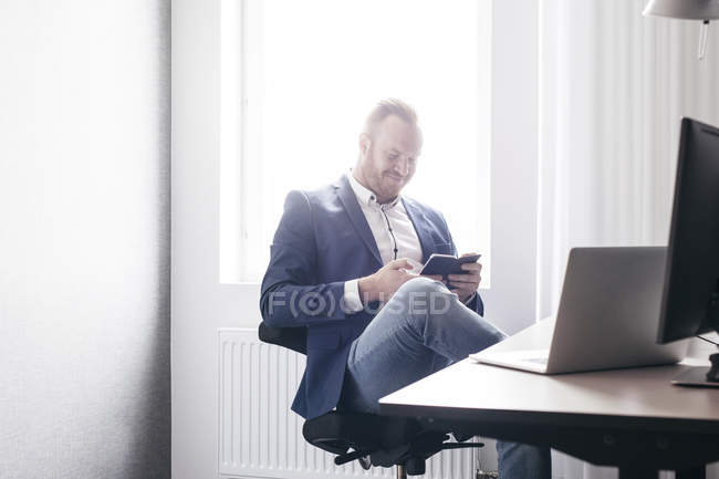 Чоловік сидить в офісі зі смартфоном — стокове фото