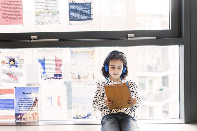 Girl sitting on window sill with headphones — Stock Photo