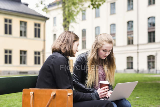 Dos estudiantes sentados en el patio de la escuela con portátil y taza de café - foto de stock