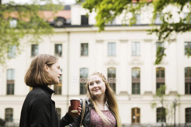 Два студента разговаривают во дворе университета за чашкой кофе — стоковое фото