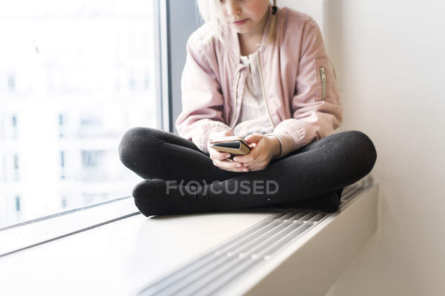 Menina sentada no peitoril da janela com smartphone — Fotografia de Stock