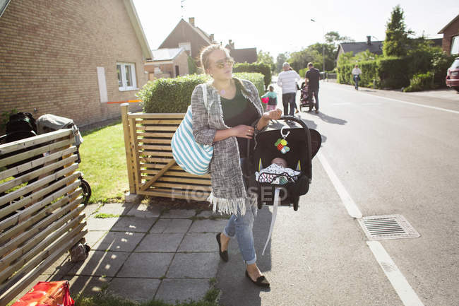 Mère portant le fils de bébé dans le siège d'auto portable avec des personnes méconnaissables en arrière-plan — Photo de stock