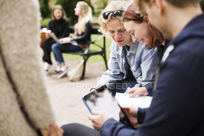 Grupo de alunos sentados e conversando no pátio da universidade com tablet digital — Fotografia de Stock