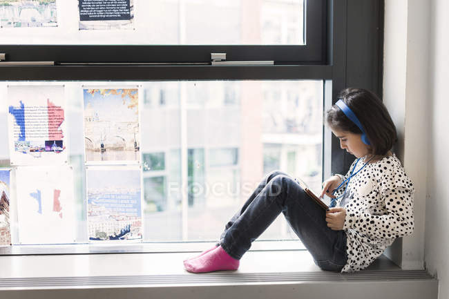 Menina sentada na soleira da janela com fones de ouvido — Fotografia de Stock