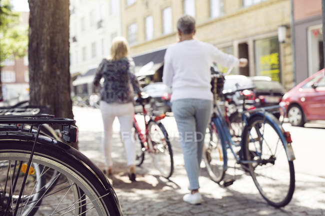 Mujeres empujando bicicletas en la ciudad - foto de stock