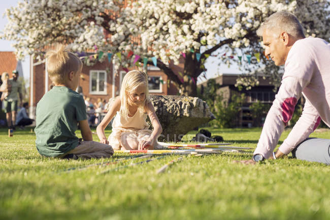 Vater spielt mit Tochter und Sohn im Garten mit riesigen Stöcken — Stockfoto
