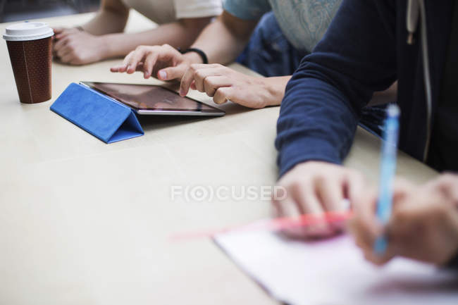Крупним планом студенти пишуть нотатки і працюють з цифровим планшетом — стокове фото