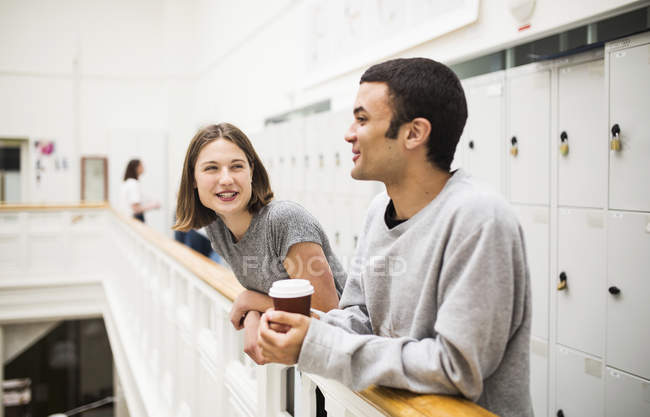 Dos estudiantes de pie junto a la barandilla frente a los armarios con café - foto de stock