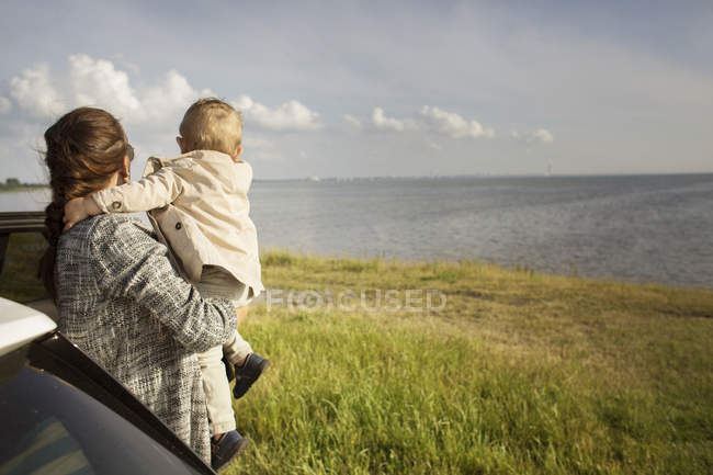 Madre sosteniendo hijo cerca de la puerta del coche - foto de stock