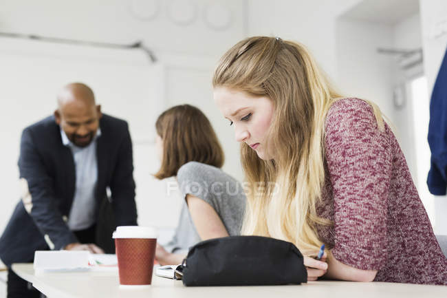 Students studying at desk in classroom with teacher — Stock Photo