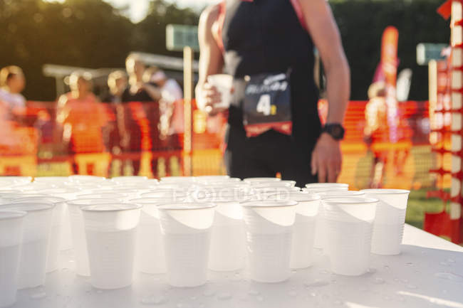 Table with cups of water at sports event with unrecognizable peopleinbackground — Stock Photo