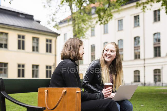Двоє студентів сидять на шкільному подвір'ї з ноутбуком та чашкою кави — стокове фото