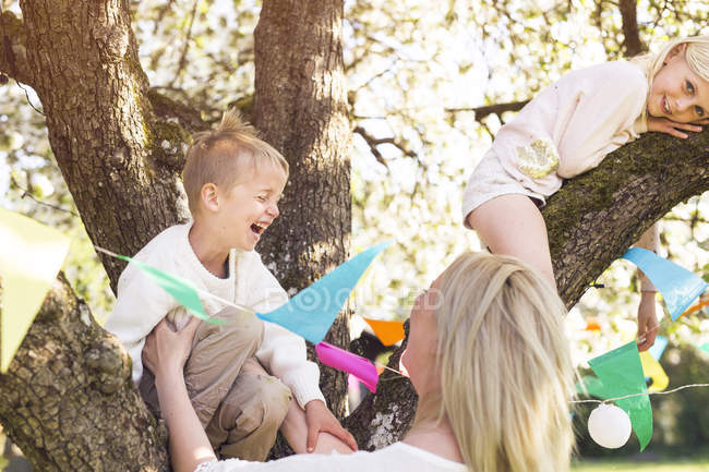 Garçon et fille jouant sur les branches d'arbre avec la mère — Photo de stock