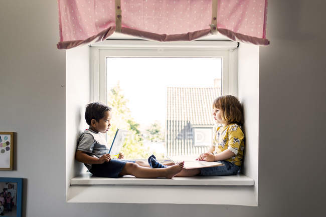 Niños sentados en alféizar ventana - foto de stock