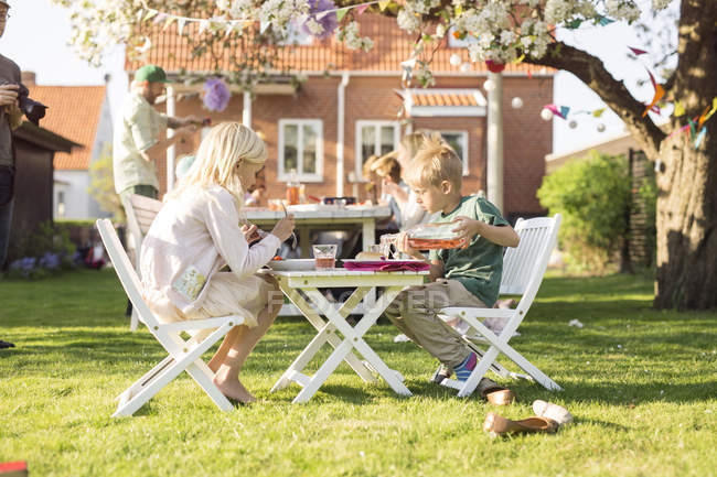 Діти сидять за маленьким столом для пікніка в саду — стокове фото