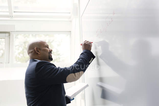 Teacher writing on whiteboard in classroom — Stock Photo