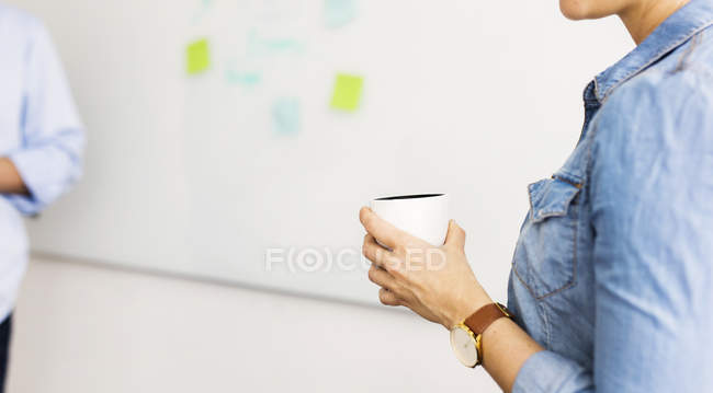 Ausgeschnittene Ansicht einer Frau, die Tasse vor Whiteboard hält — Stockfoto