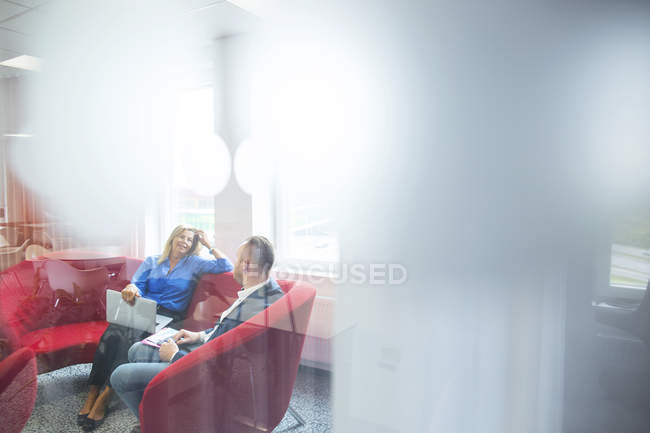 Коллеги сидят на красном диване и разговаривают — стоковое фото
