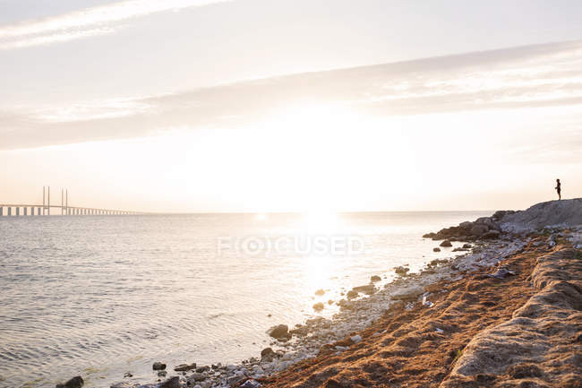 Человек на скалистом побережье на закате — стоковое фото