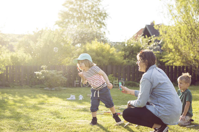 Femme et enfants soufflant des bulles dans le jardin — Photo de stock