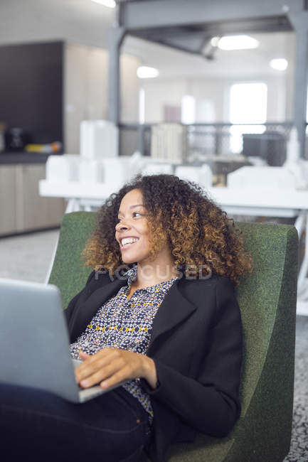 Mujer sonriendo mientras usa el ordenador portátil - foto de stock