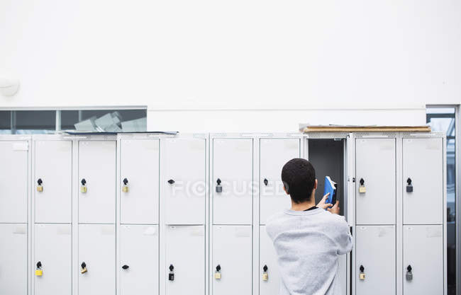Rear view of student putting book into locker — Stock Photo