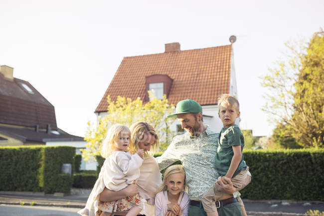 Семья с тремя детьми стоит перед домом в пригороде — стоковое фото