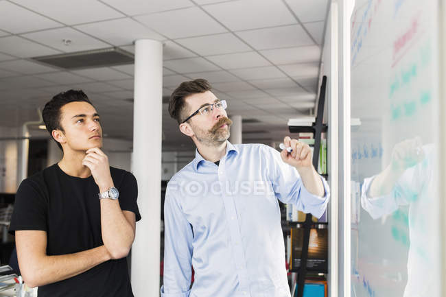 Kollegen stehen im Büro neben Whiteboard und schauen auf — Stockfoto