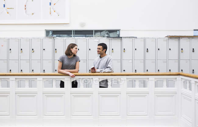 Dos estudiantes de pie junto a la barandilla frente a los armarios con café - foto de stock
