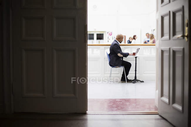 Teacher sitting at desk with laptop with students in background — Stock Photo