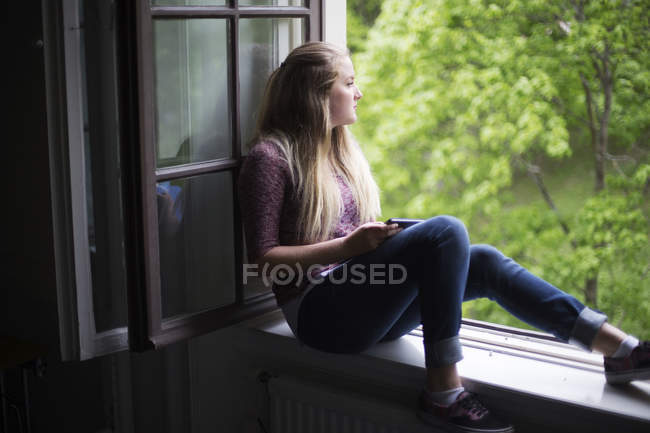 Female student sitting on window sill with digital tablet — Stock Photo