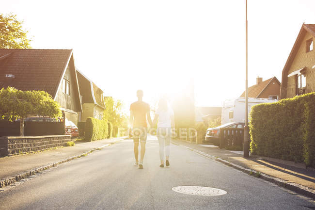 Vue arrière d'un jeune couple marchant sur une route de banlieue — Photo de stock
