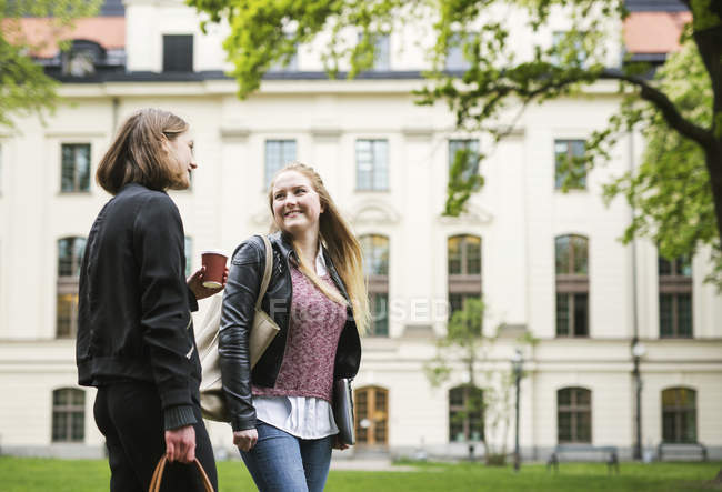 Two students talking in university yard with cup of coffee — Stock Photo