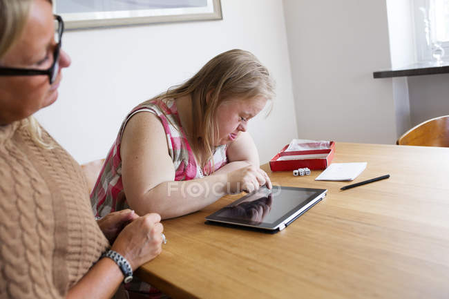 Filha com síndrome de down usando tablet digital, mãe olhando — Fotografia de Stock