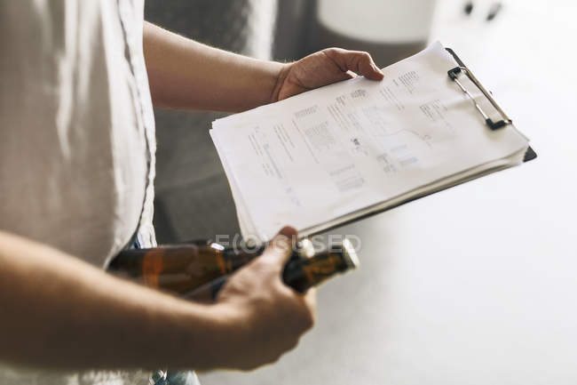 Mid section of brewery worker holding documents and beer — Stock Photo