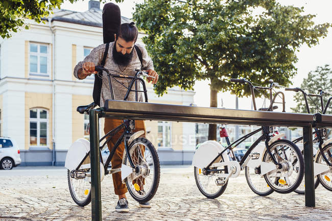 Hombre tomando bicicleta de alquiler fuera de rack en la estación - foto de stock