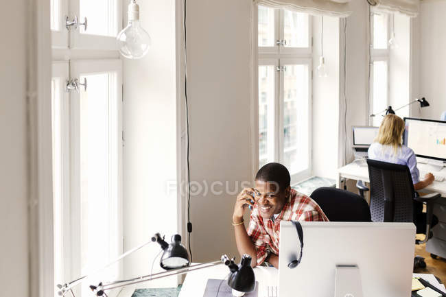 Homme parlant au téléphone, femme utilisant un ordinateur au bureau — Photo de stock
