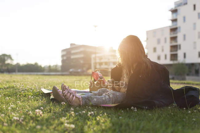 Девушка (4-5) сидит на траве и пользуется телефоном — стоковое фото