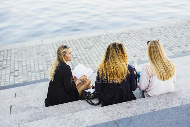 Três jovens mulheres sentadas em degraus junto ao rio — Fotografia de Stock
