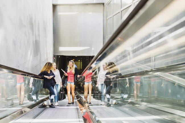 Three young women on escalator — Stock Photo