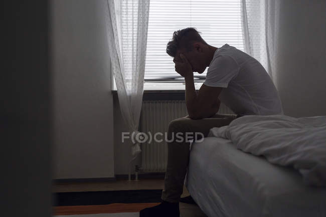 Nachdenklicher junger Mann sitzt auf Bett — Stockfoto