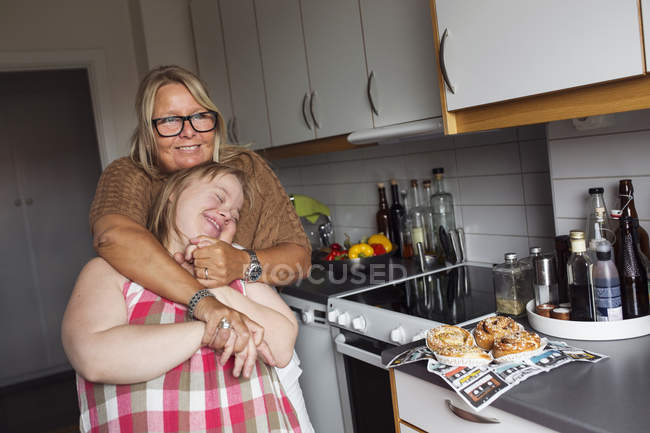Mãe abraçando filha com síndrome de down na cozinha — Fotografia de Stock