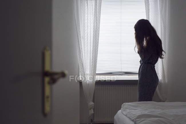 Pensive jeune femme debout près de la fenêtre — Photo de stock