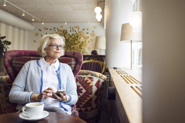 Femme âgée regardant par la fenêtre pendant la pause café dans le café — Photo de stock