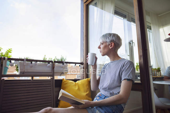 Mujer leyendo libro en balcón y bebiendo café - foto de stock