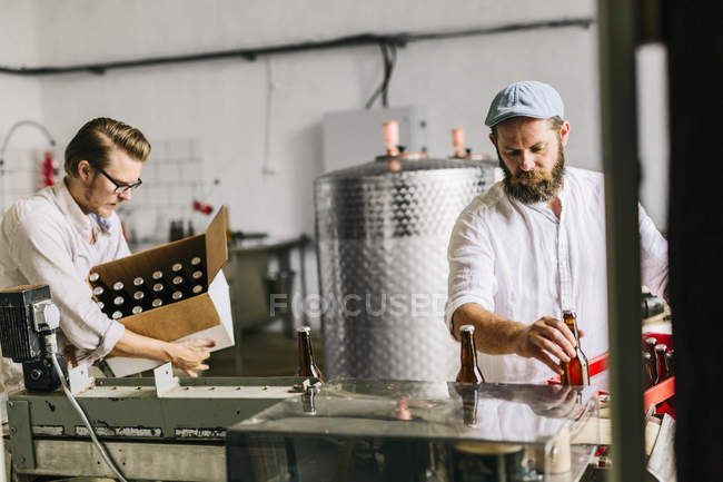 Travailleurs de brasserie mettant des bouteilles de bière dans des boîtes — Photo de stock