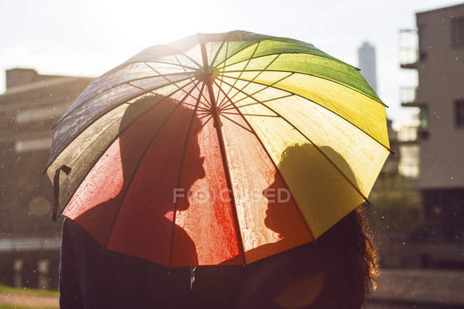 Mid casal adulto de pé sob guarda-chuva colorido ao pôr do sol — Fotografia de Stock