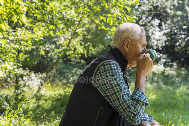 Чоловік п'є з чашки в лісі — стокове фото
